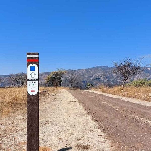 Tótem rectangular con placa ovalada indicando por dónde va el sendero.